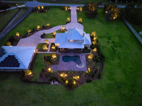 Aerial view of illuminated house with pool at night.