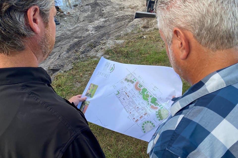 Two men examining architectural blueprint outdoors.