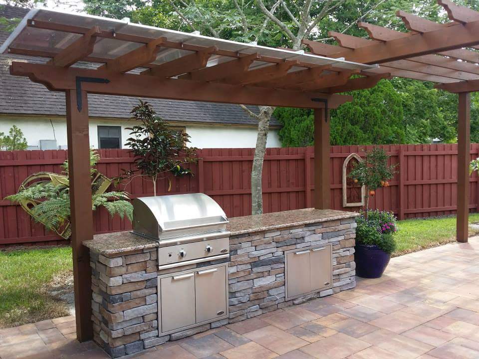 Outdoor kitchen with grill under pergola.