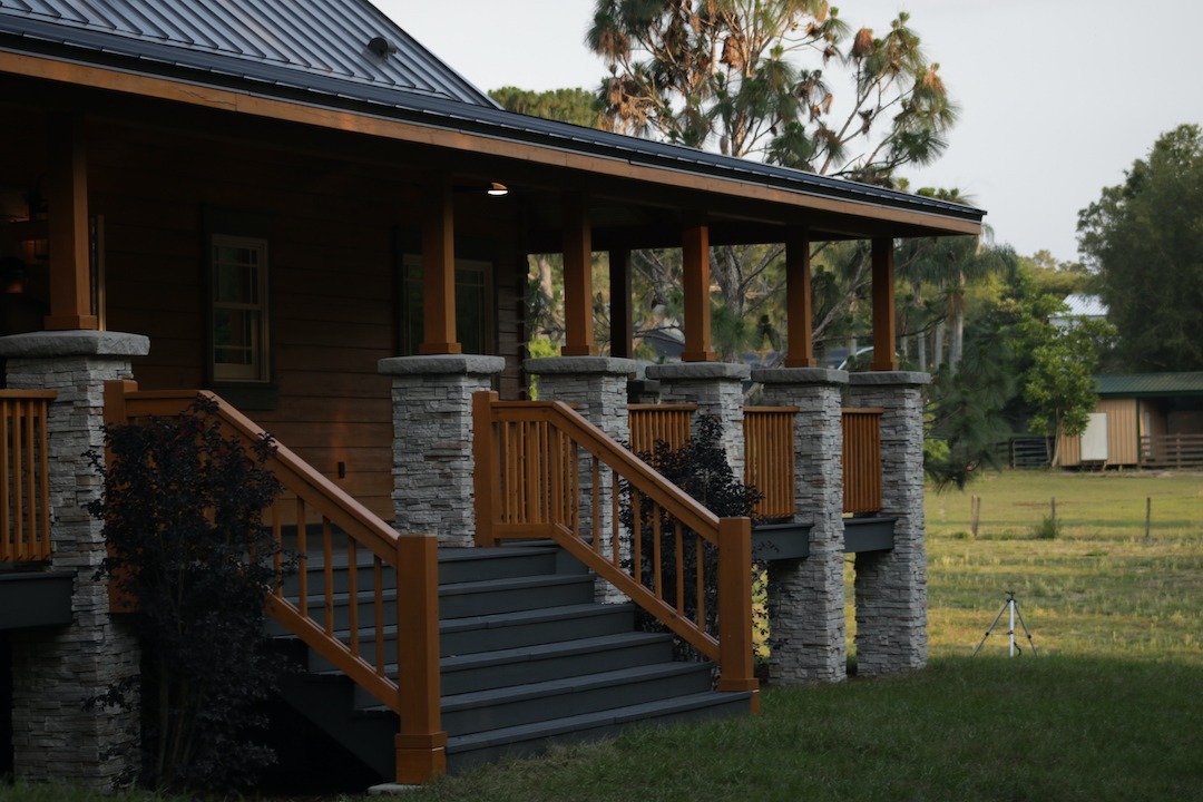 Modern farmhouse porch with stone columns and railing.