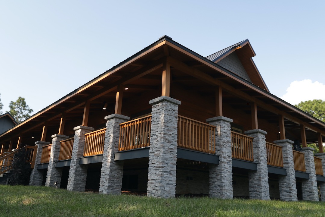 Modern wooden cabin with stone pillars, sunny day.