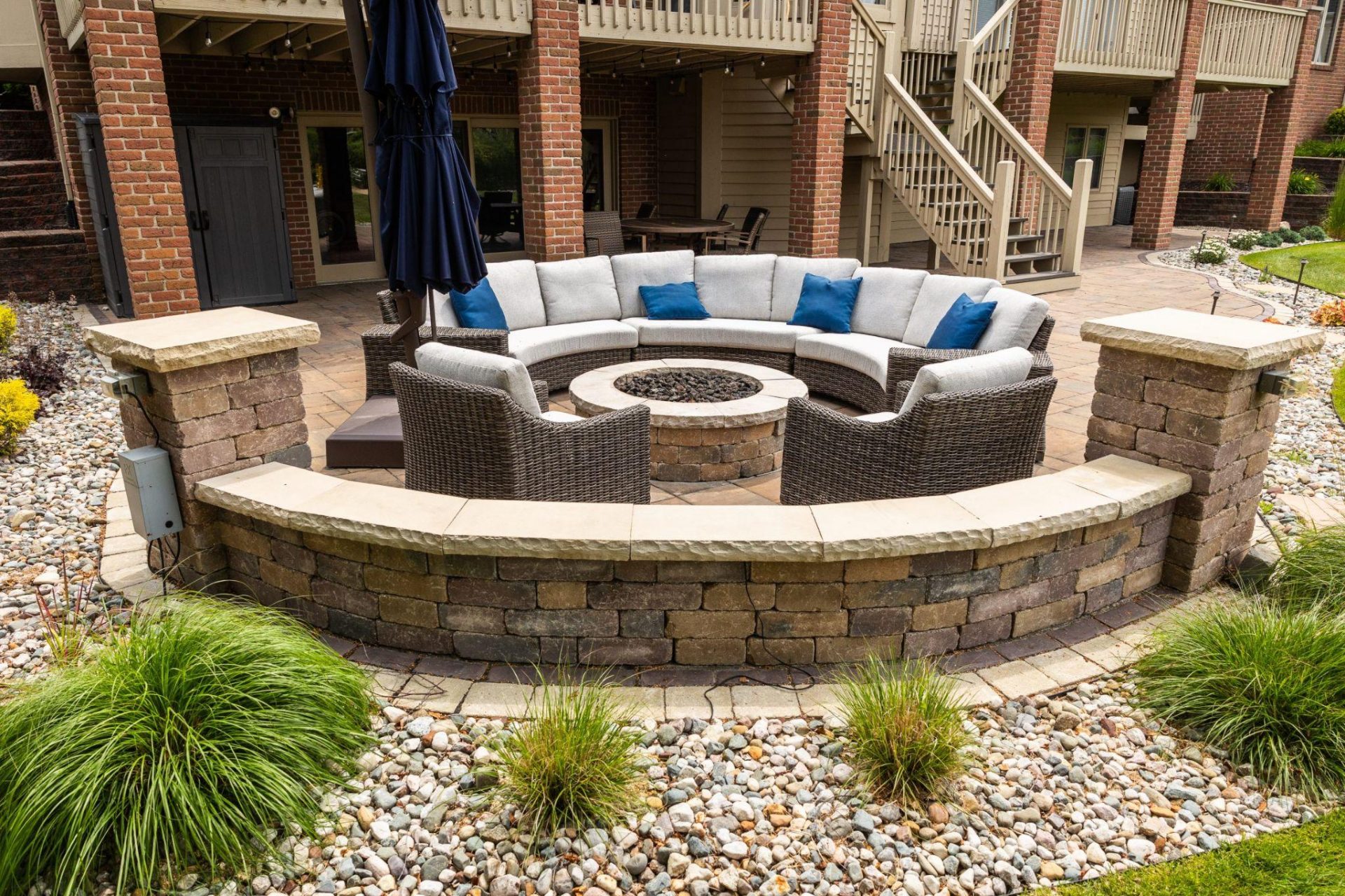Circular outdoor seating area with built-in stone fire pit, curved seating wall, and paver patio in a residential backyard.