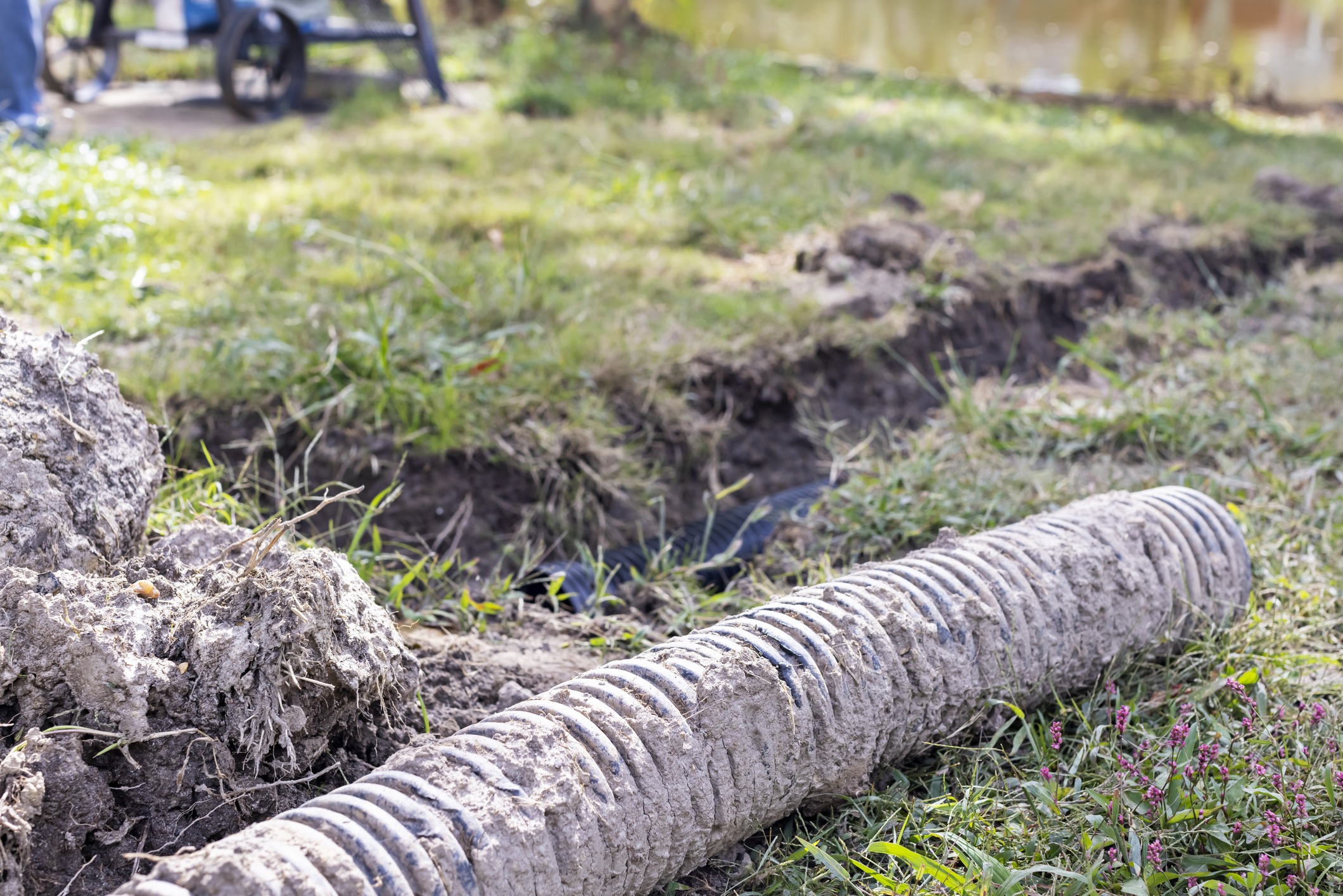 Corrugated pipe laying on grass near trench.