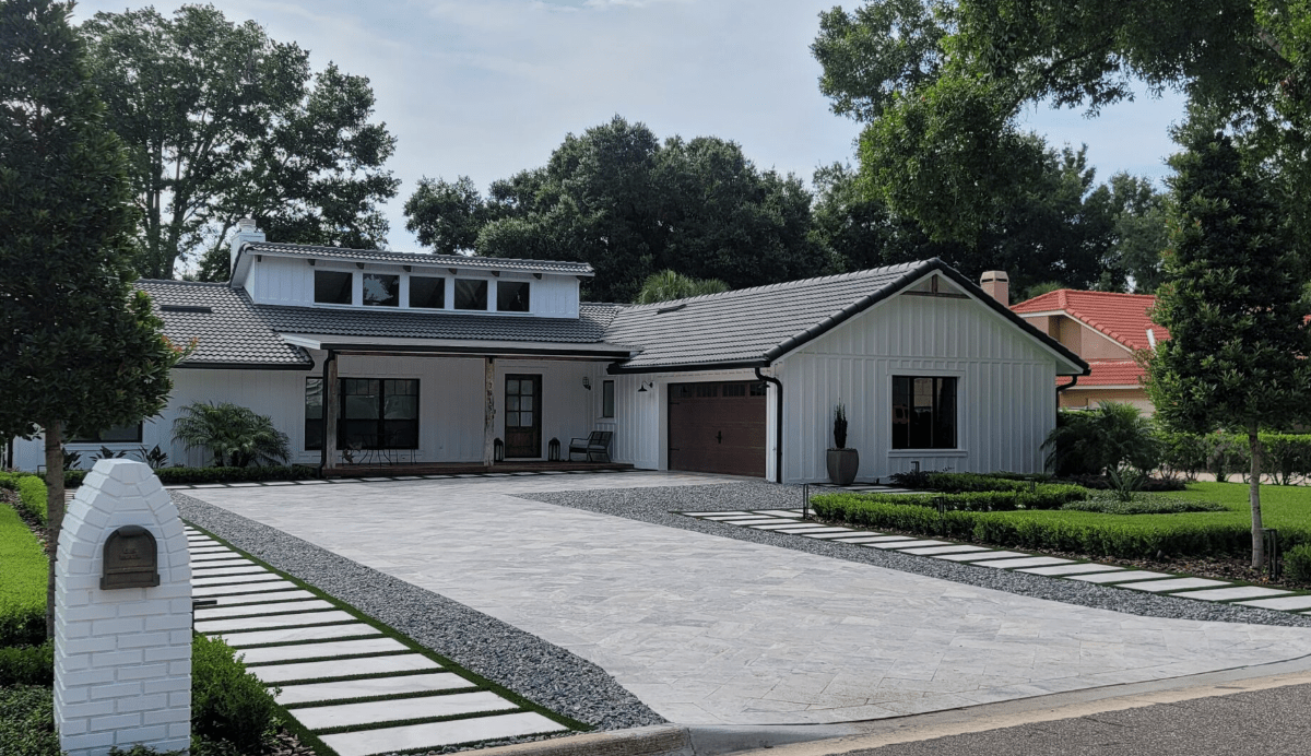 Modern farmhouse-style home with a large paver driveway, garage, and minimalist landscaping.