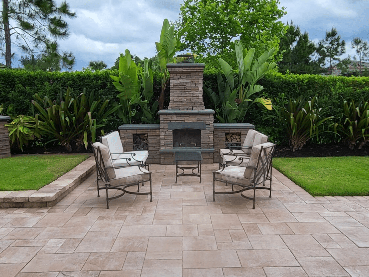 Outdoor patio with stone fireplace, cushioned chairs, and symmetrical landscaping.