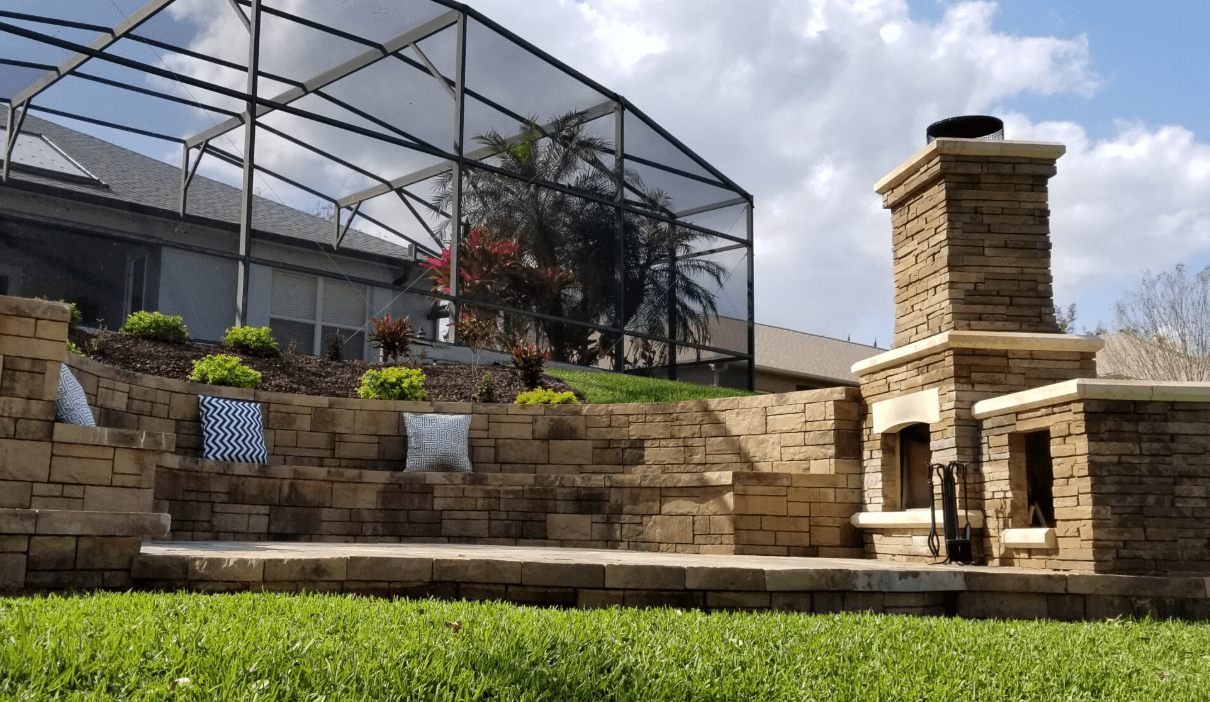 Tiered stone retaining walls with built-in seating and a custom outdoor fireplace in a landscaped backyard.